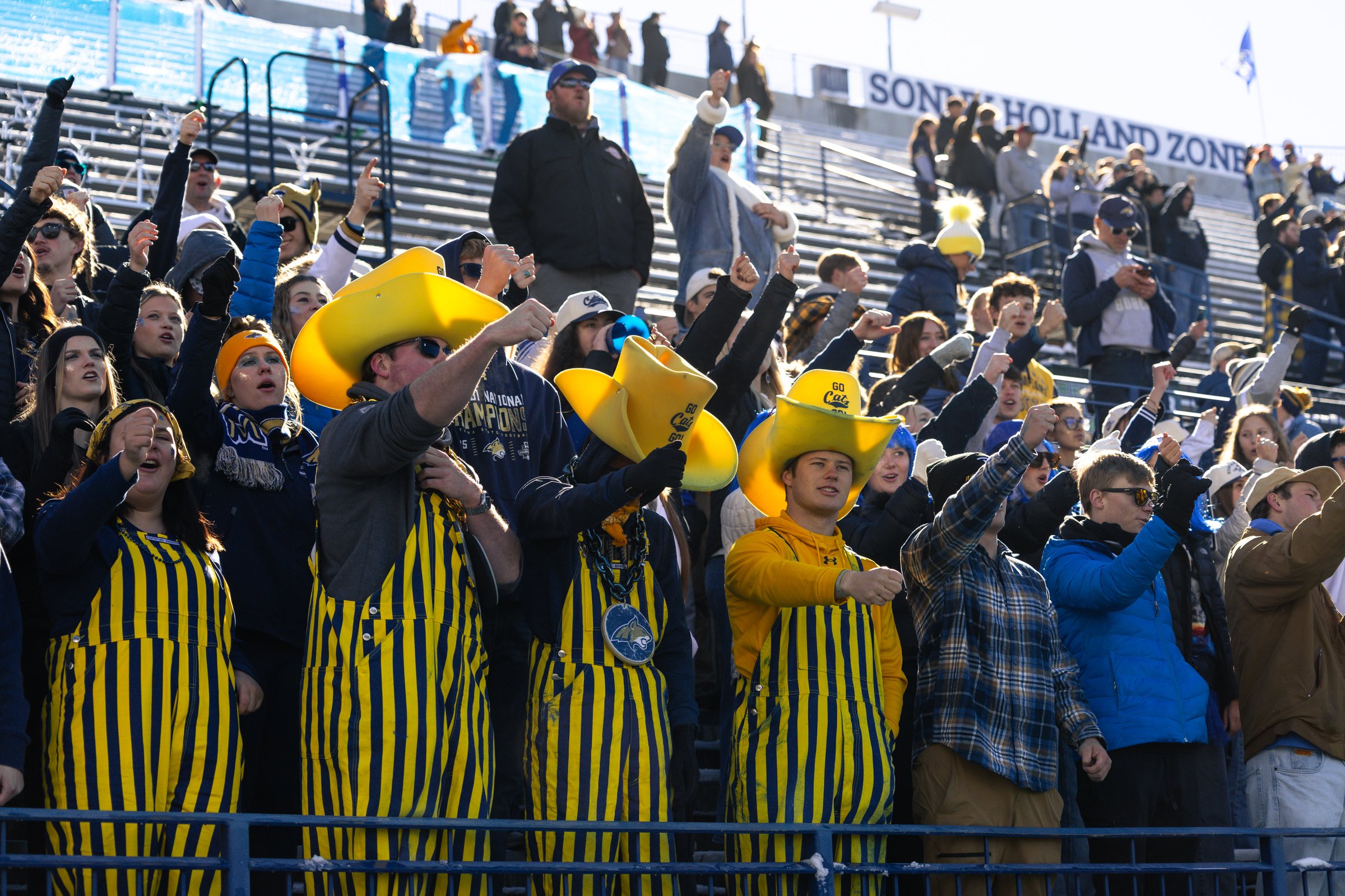 Bobcat students in striped overalls and cowboy hats cheer before kickoff