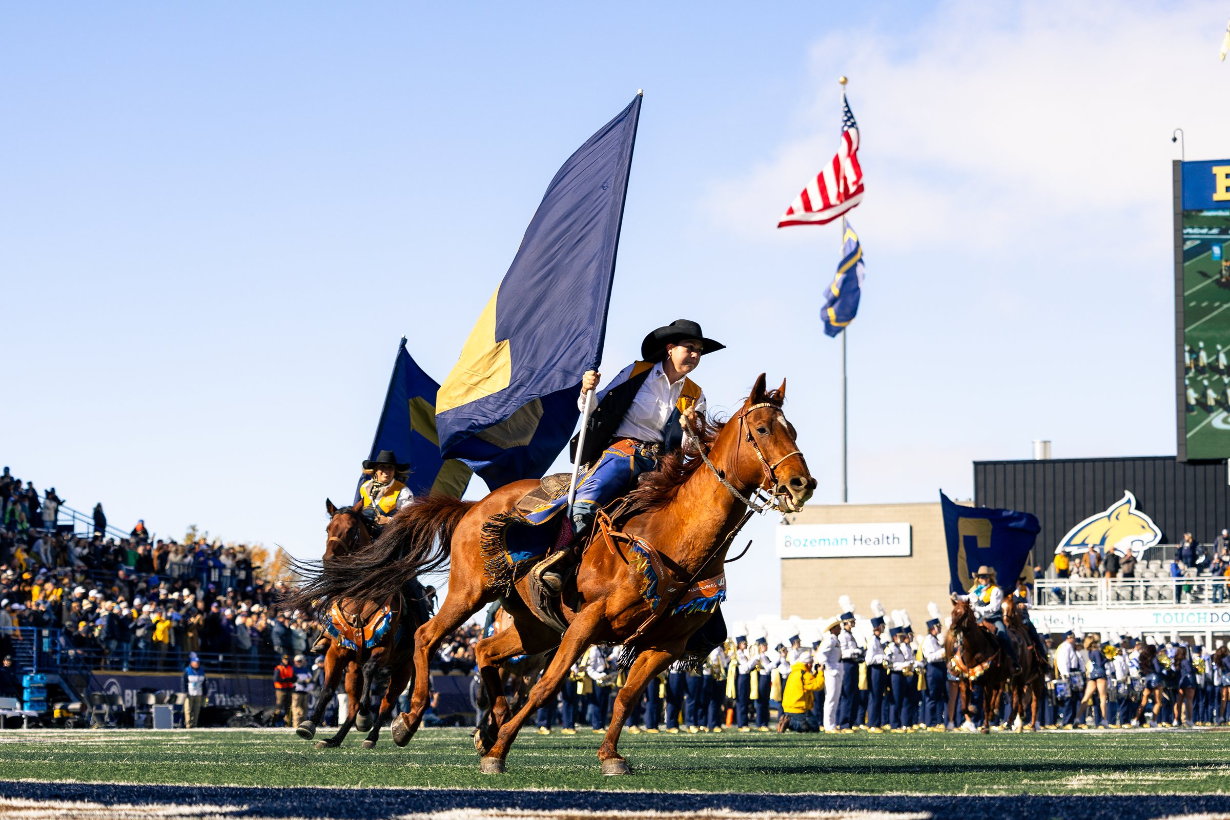 Bobcat riders carry flags across the field
