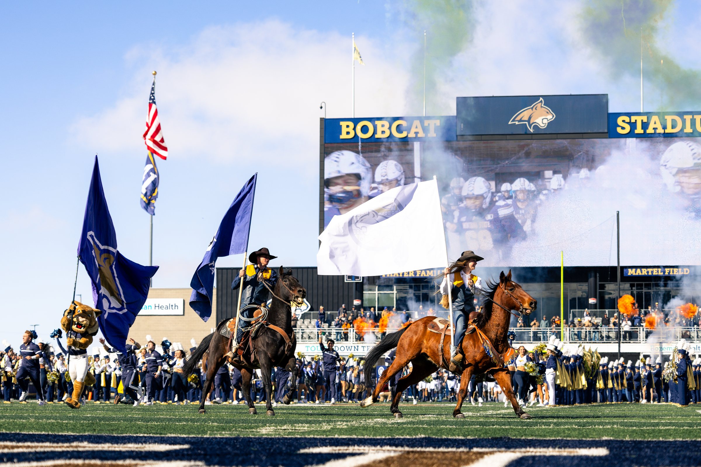 Bobcat riders and Champ lead the flags through the smoke